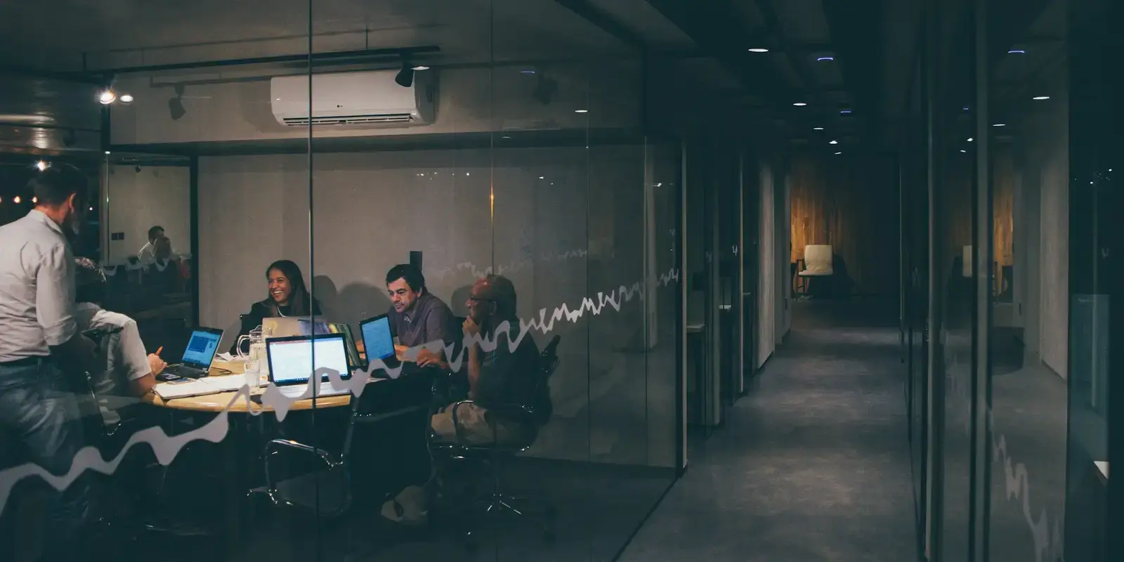 Sala de reuniones acristalada iluminada dentro de una oficina en penumbra