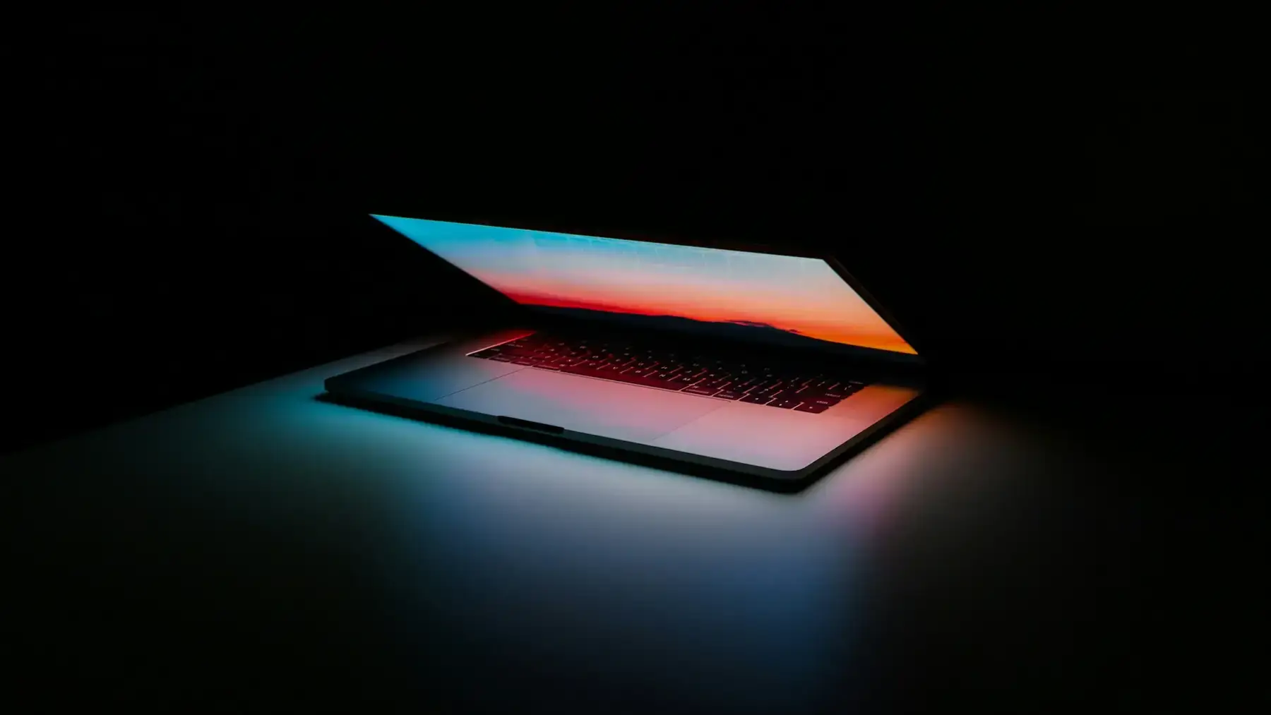 Portátil entreabierto en una sala oscura con la pantalla proyectando luz azul